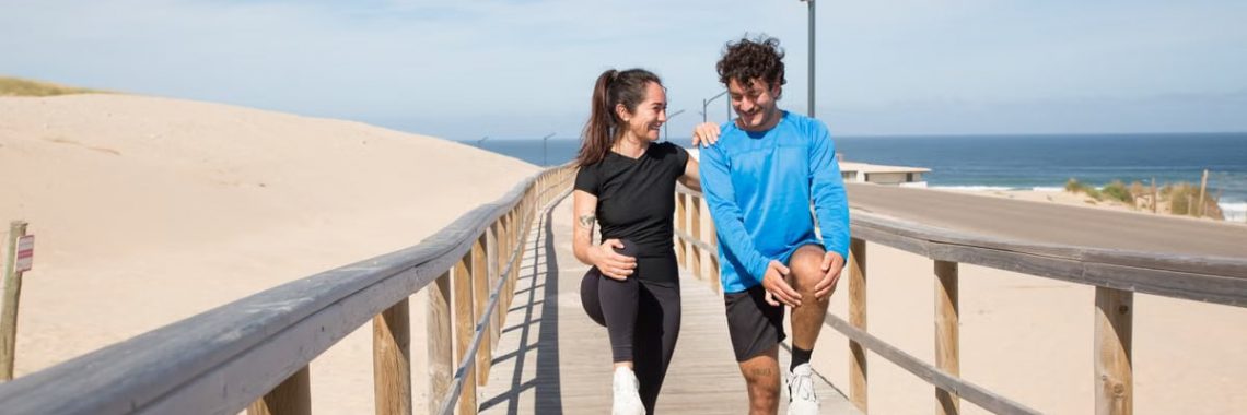 A young couple doing warm-up exercises on a boardwalk by the beach, enjoying a healthy lifestyle outdoors.